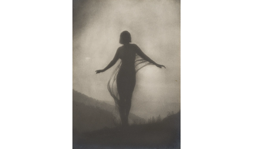 black and white photo featuring a silhouette of a figure, presumably a woman, with their arms raised slightly standing outdoors