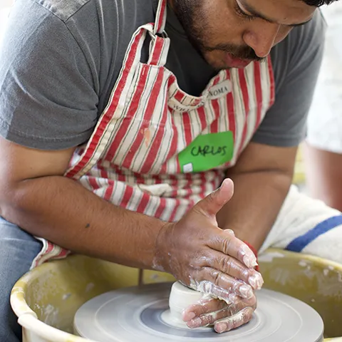 a bearded man wearing an apron working on ceramics at a potters wheel 