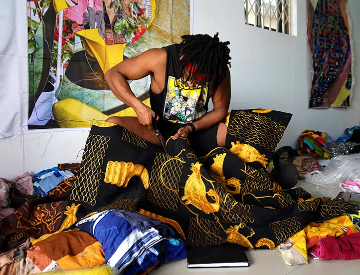 photo of a seated Black man in a dark cutoff tee cutting ornate fabric