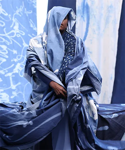 photo of a dark skinned person wrapped in indigo colored material against indigo colored fabric backdrop