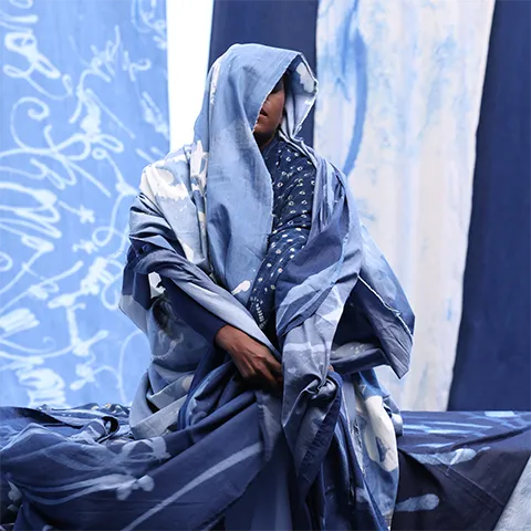 photo of a dark skinned person wrapped in indigo colored material against indigo colored fabric backdrop