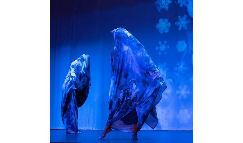 fabric draped individuals on stage with a backdrop featuring abstract symbols and everything is lit in varying shades of blue