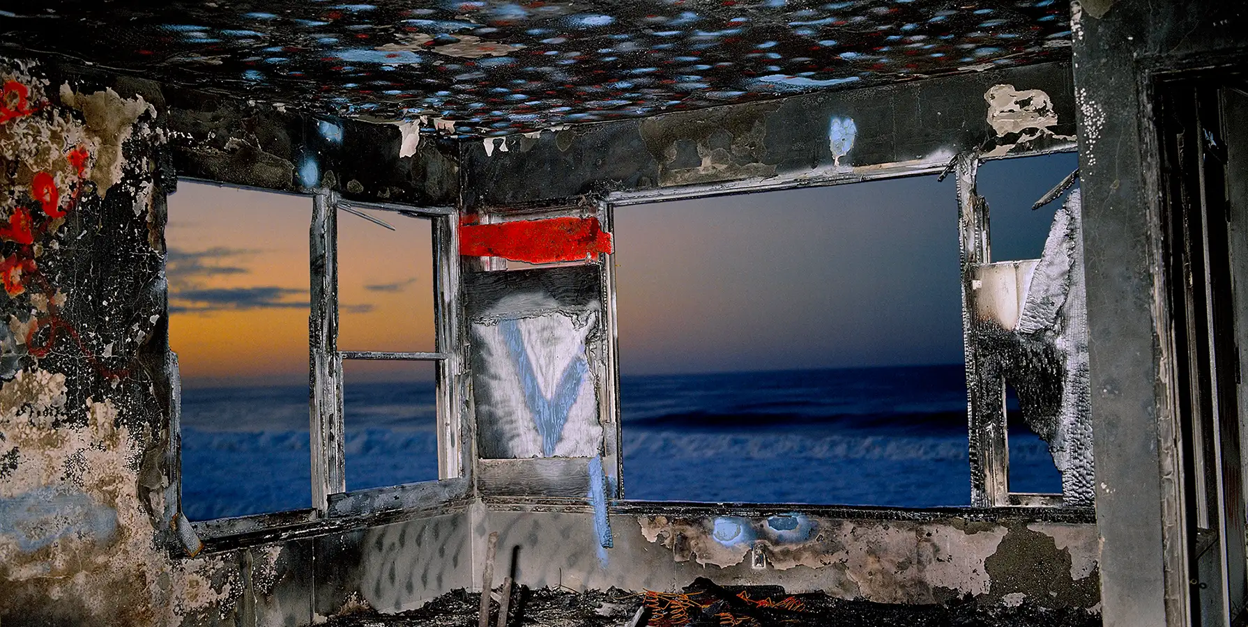 photo of a burned interior of a building with a view of the shore at dawn through windows