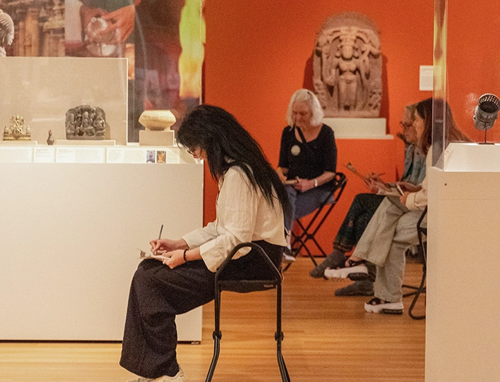 seated museum visitors sketching in the Asian gallery surrounded by art