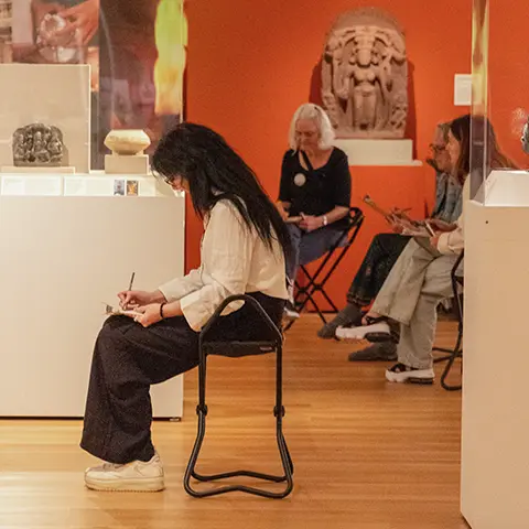 seated museum visitors sketching in the Asian gallery surrounded by art
