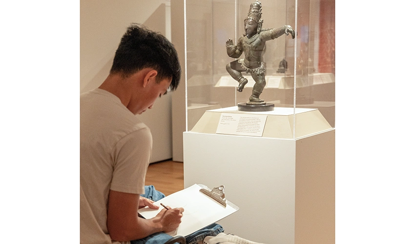 museum guest sketching in front of a statue in the Asian gallery