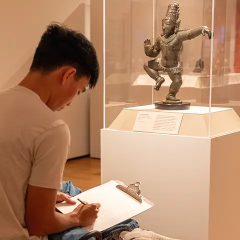 museum guest sketching in front of a statue in the Asian gallery