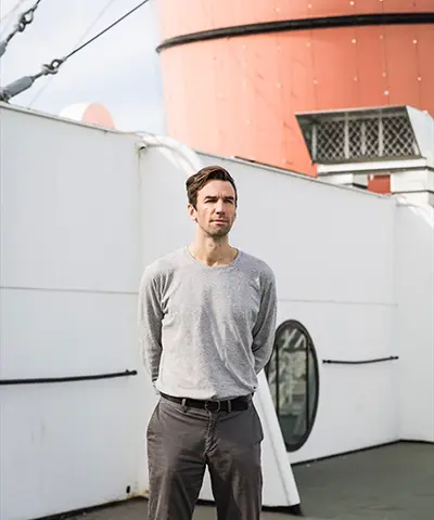 a man in casual clothes aboard a ship facing the viewer