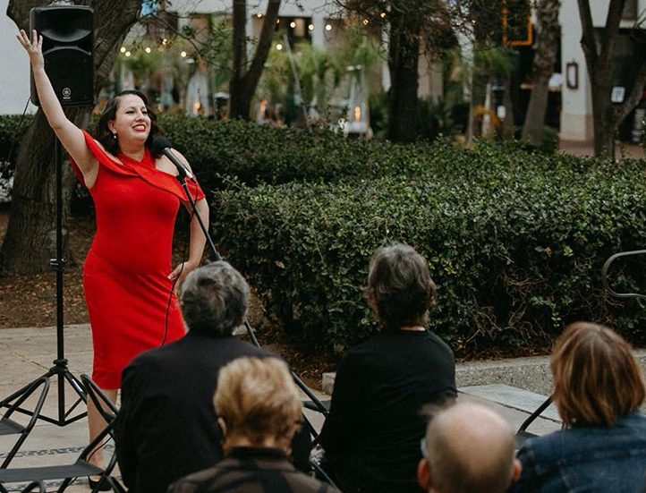 singer in a red dress posing with her arm raised in front of a crowd on terrace