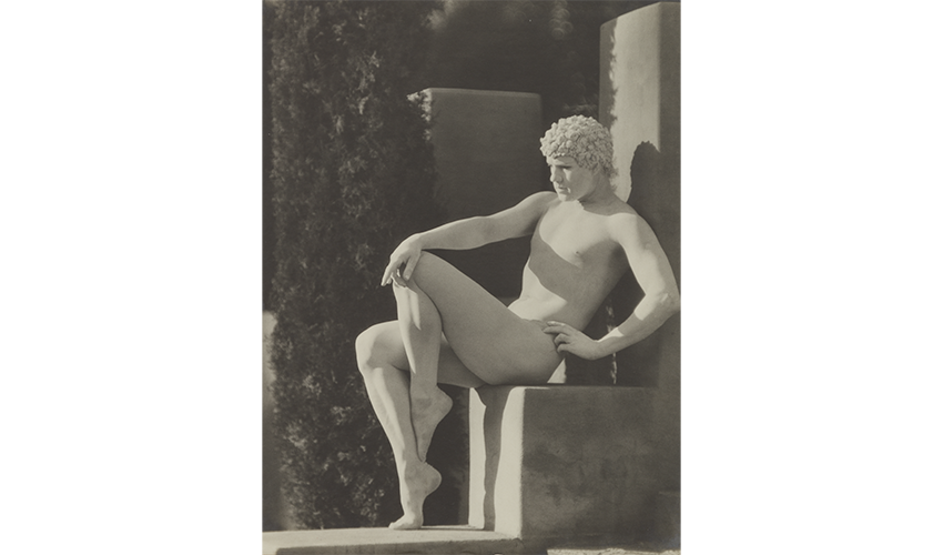 a seated nude man painted white and strategically posed resembling a marble statue