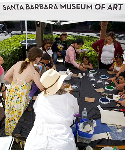 people crafting around a long black table outside under a white tent