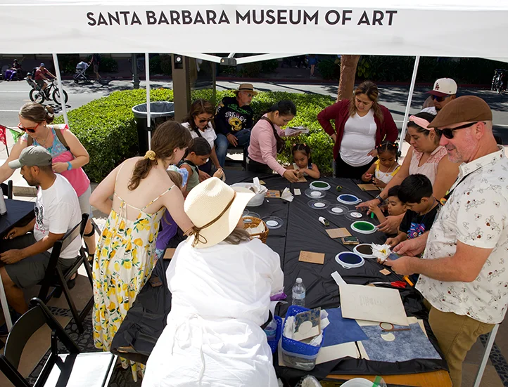 people crafting around a long black table outside under a white tent