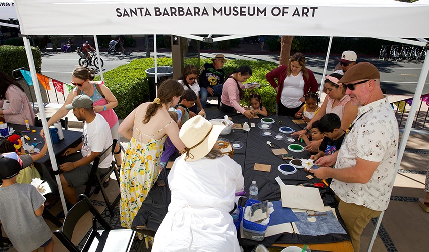 people crafting around a long black table outside under a white tent