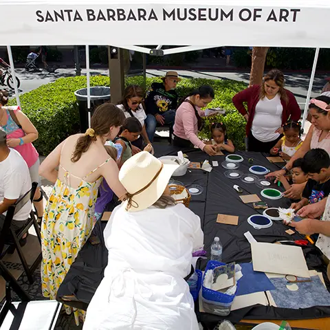 people crafting around a long black table outside under a white tent