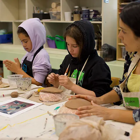 young people working with clay at a table led by an instructor