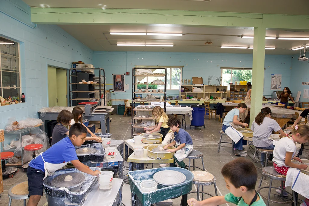 several kids working in a classroom of pottery wheels