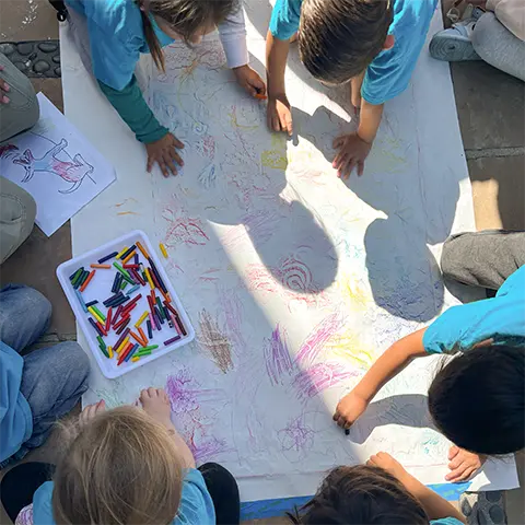 view from above of several kids working with crayons on a big piece of paper