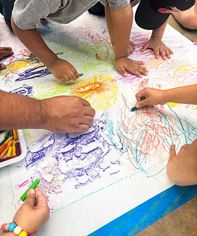 view from above of several pairs of hands working with crayons on a big piece of paper
