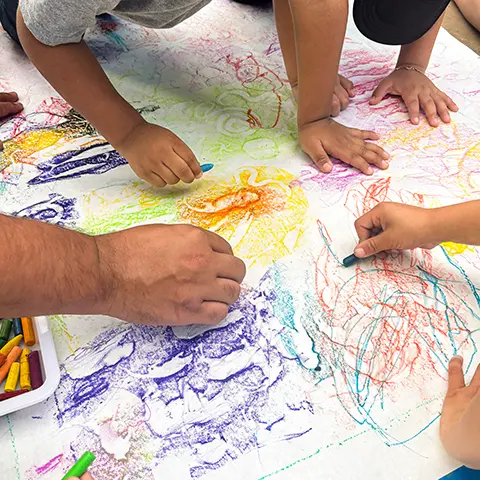 view from above of several pairs of hands working with crayons on a big piece of paper