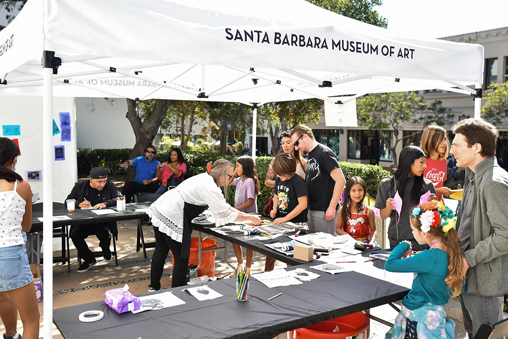people under a white santa barbara museum of art tent working a festive event
