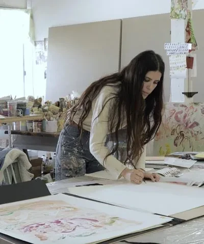 photo of the artist working in her studio, bent over a table drawing