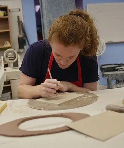 photo of student wearing a red apron crafting at a table