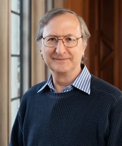headshot of a scholar with short gray hair and glasses wearing a dark sweater over a collared shirt