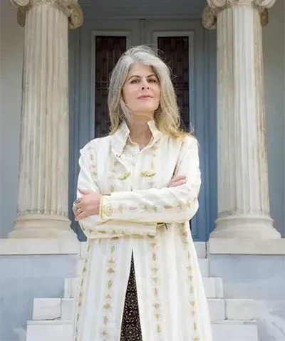 photo of a woman in a white coat with her arms crossed standing in front of an old structure with big columns