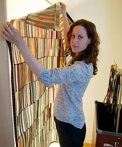 photo of an artist looking into the lens while holding up a colorful artwork against a lightbox