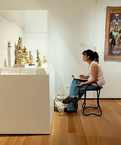 photo of a seated student sketching Asian art in a gallery