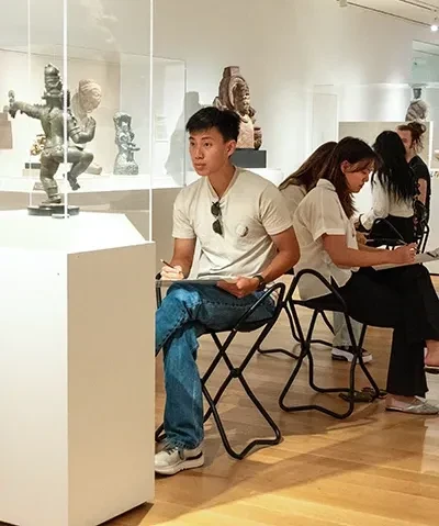 group of seated students drawing in a gallery of Asian art