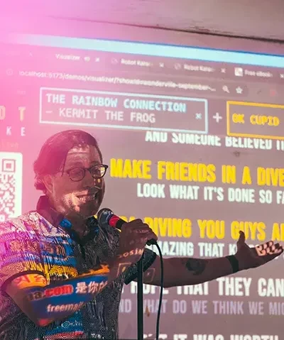 photo of a man in front of a screen being projected with lyrics and graphics speaking into a microphone