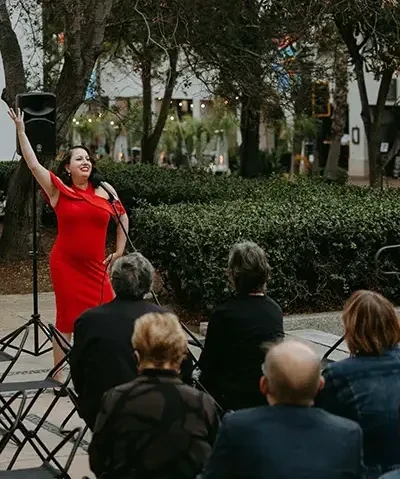 singer in a red dress posing with her arm raised in front of a crowd on terrace