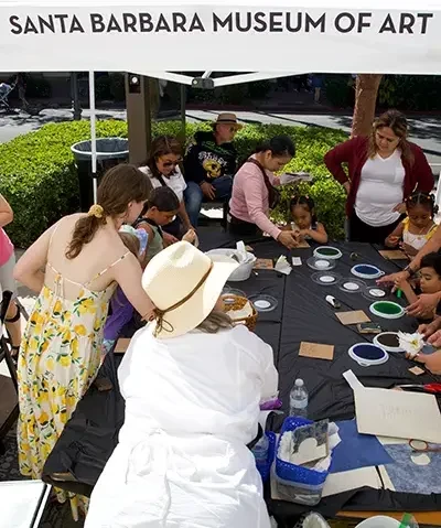 people crafting around a long black table outside under a white tent