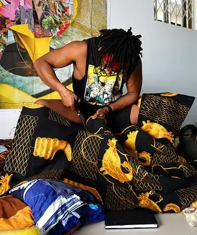 photo of a seated Black man in a dark cutoff tee cutting ornate fabric