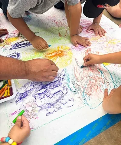 view from above of several pairs of hands working with crayons on a big piece of paper