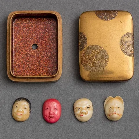 photo of four figural netsukes with open case lying flat on gray table 