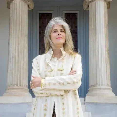 photo of a woman in a white coat with her arms crossed standing in front of an old structure with big columns