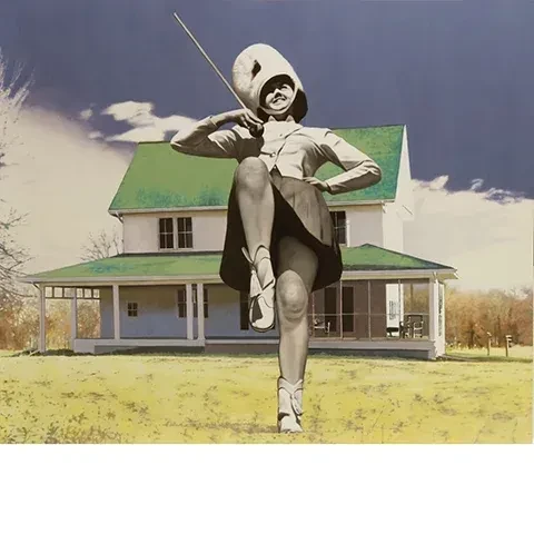 color image of a farm house with a green roof with an oversized majorette rendered in black and white in the foreground