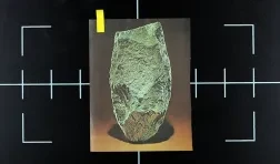 video still of a black surface with white registration marks and an image of a green stone artifact layed on top