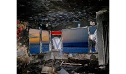 photo of a burned interior of a building with a view of the shore at dawn through windows